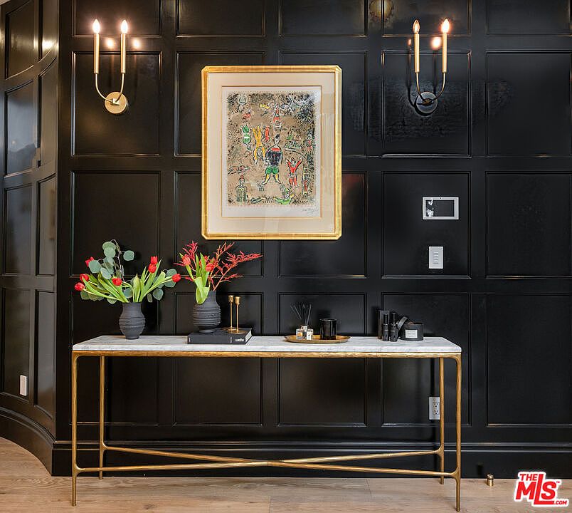 Foyer with floor-to-ceiling black panelled walls, brass sconces, and a marble-topped console.