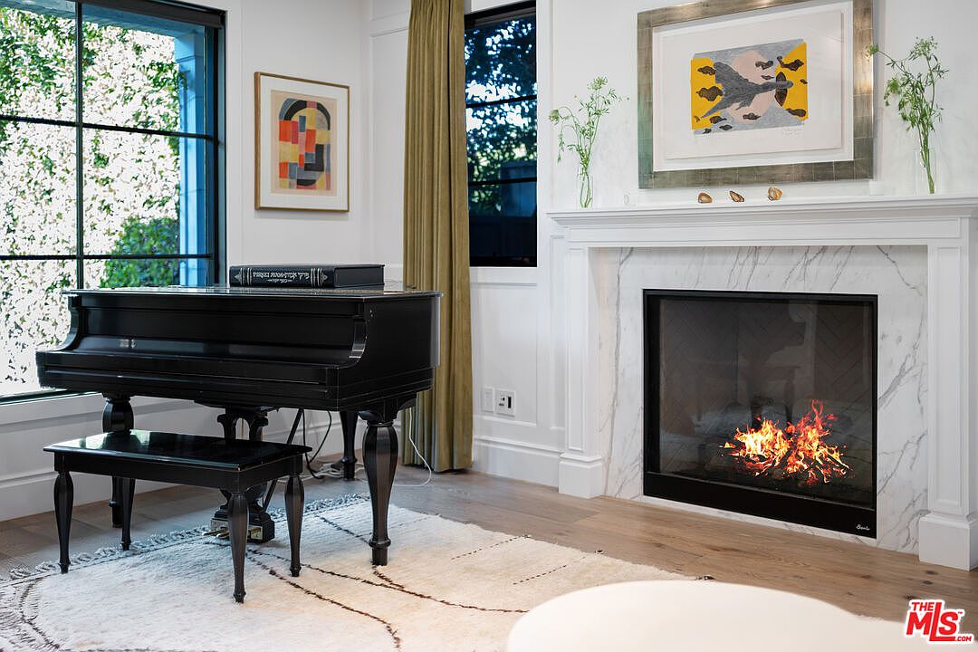 Living room with marble fireplace lit, a black grand piano, and tall garden-facing windows.