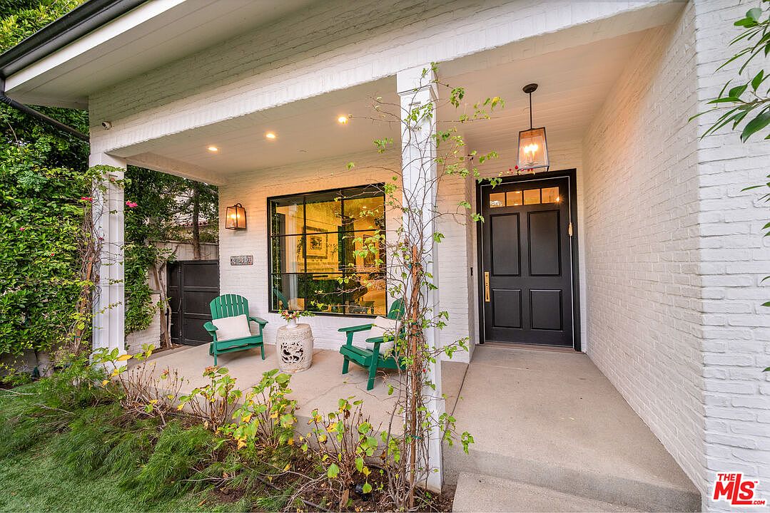 Covered front porch with brick walls, a black entry door, and a pair of green Adirondack chairs.