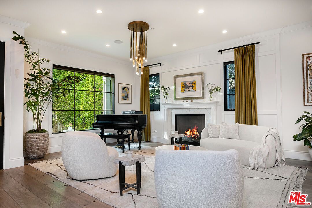Sitting room with bouclé chairs, a brass chandelier, and the marble fireplace anchoring the long view.